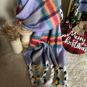 Colorful plaid scarf with tassels displayed on carpet near holiday decor.